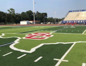 The Sabine Cardinals logo on the James Bamberg Stadium turf. Sabine is in the deep end of the pool, so to speak, in the 2024 schedule: eight of its 10 opponents this year made the playoffs a year ago. But the Cardinals are used to a tough schedule, and they'll battle in what coach Cody Gilbert (below, with his family) calls the district that's "the SEC of Class 3A football in Texas." (Photos by JOE HALE - ETBLITZ.COM)