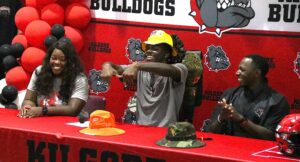 Kilgore defensive back Jayden Sanders, center, signs the Michigan "M" as mom Whitney Clark, left, and dad Nick Sanders look on Saturday morning. Jayden announced his verbal commitment to the Wolverines Saturday, following Kilgore's football photo day. (Photo by DENNIS JACOBS - ETBLITZ.COM)